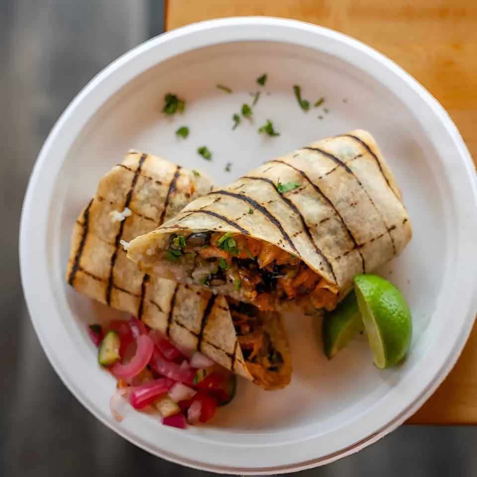 Two grilled burritos, one cut open, with lime wedges and pickled onions on a white plate.