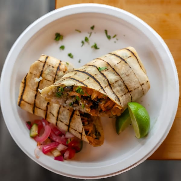 Two grilled burritos filled with rice, beans, and meat, served with lime wedges and pickled onions.