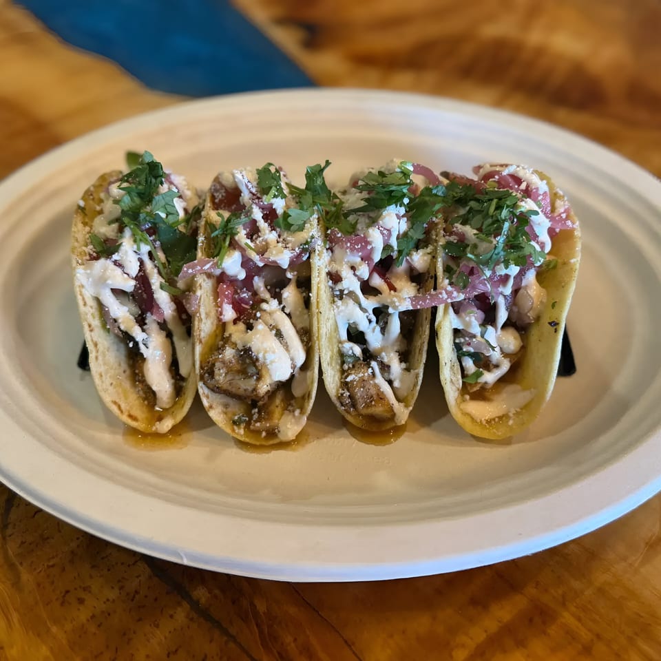 Four El Jefe's Grill Mexican BBQ tacos with meat, sauce, cilantro, and pickled onions on a white plate.