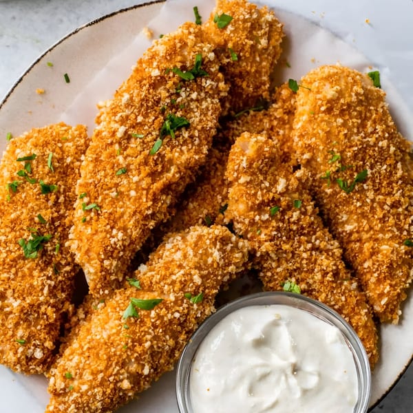 Crispy breaded chicken tenders with fresh parsley, served with a side of creamy white dipping sauce.
